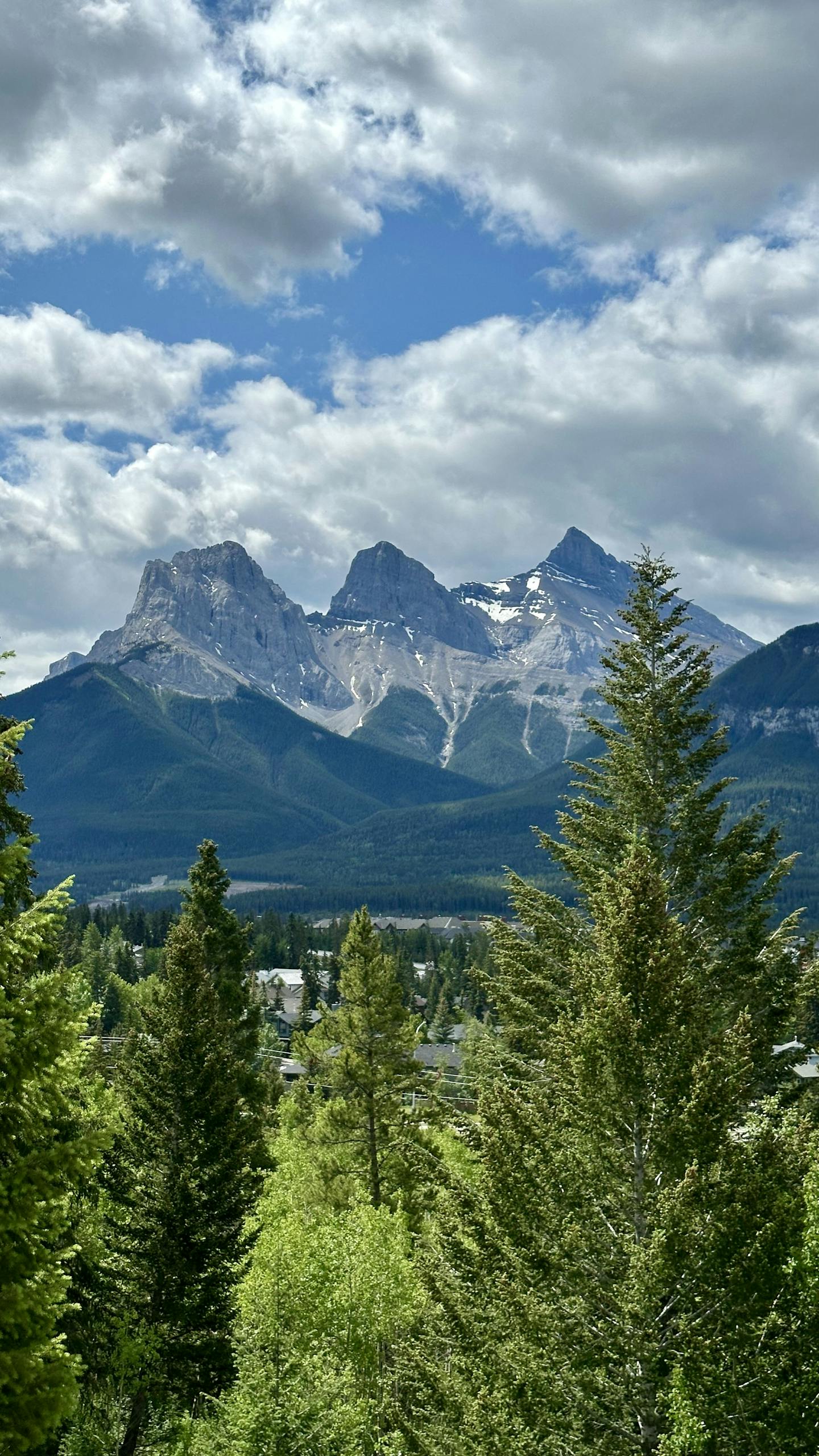 Breathtaking view of the Three Sisters mountain range in the Canadian Rockies with lush green foreground.